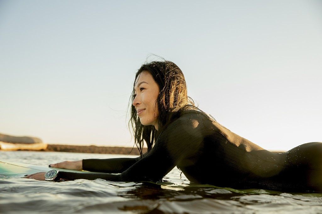 穿着绿色劳力士潜航者躺在冲浪板上的女人。